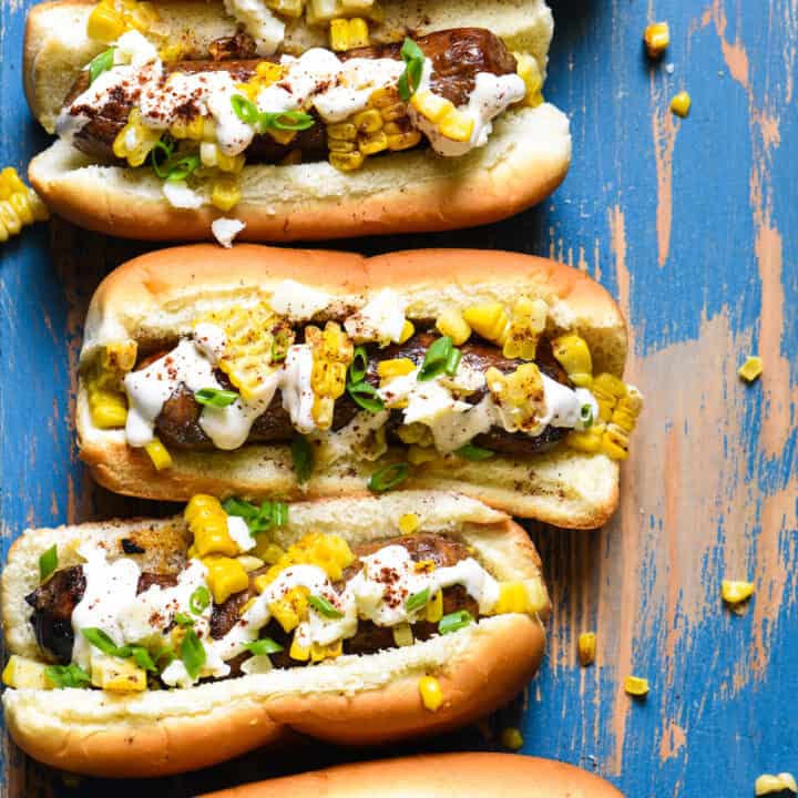 Inspired by elote, these Mexican Street Corn Brats are ideal for a summer celebration or easy weeknight meal! Spicy sausages are topped with fresh sweet corn, creamy lime sauce and tangy cheese. | foxeslovelemons.com