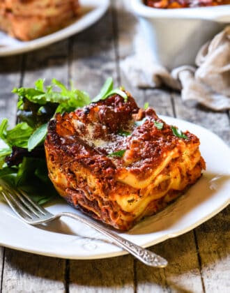 Piece of classic lasagna with cottage cheese with a side salad on a rustic white plate.