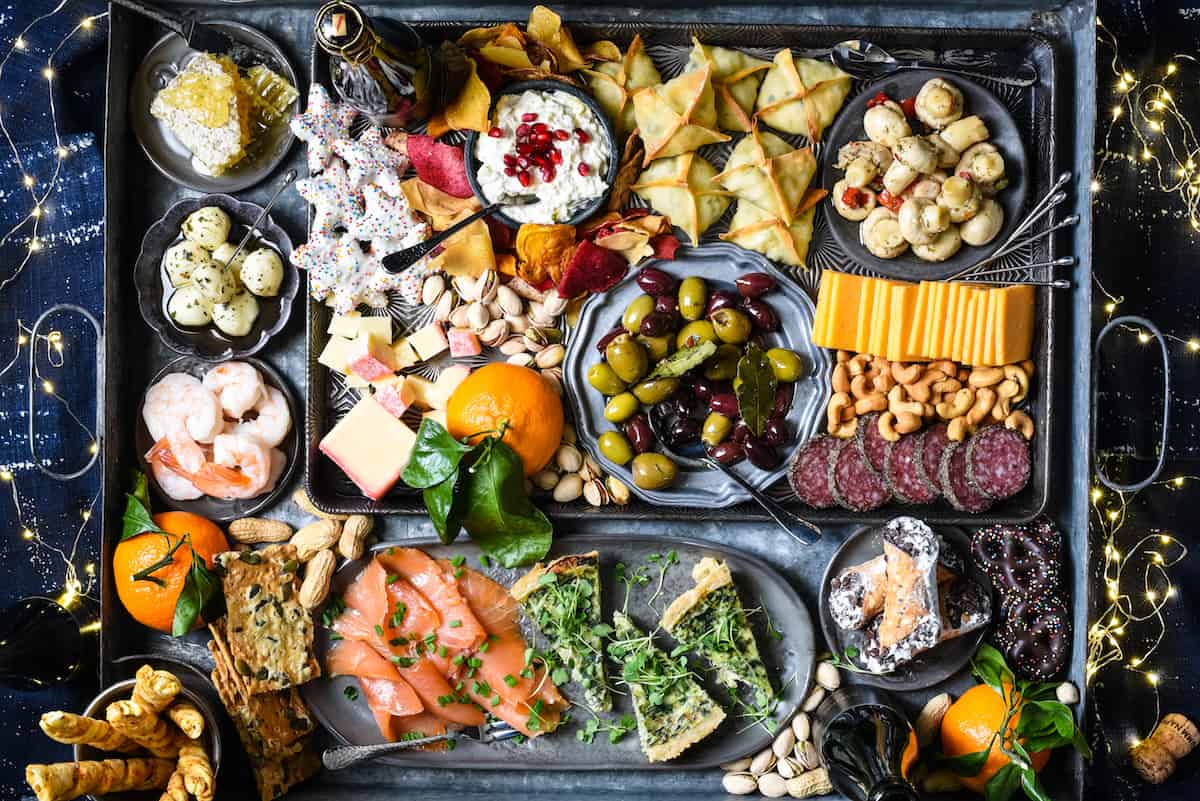 Large platter of New Years foods, including quiche, crackers, smoked salmon, salami and olives.