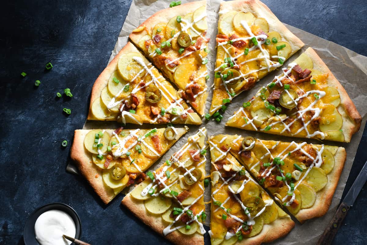 Loaded baked spud pie drizzled with ranch dressing, on dark surface.