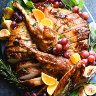 Large slate blue ceramic platter filled with a cut up roasted turkey, garnished with grapes, orange slices and herbs.