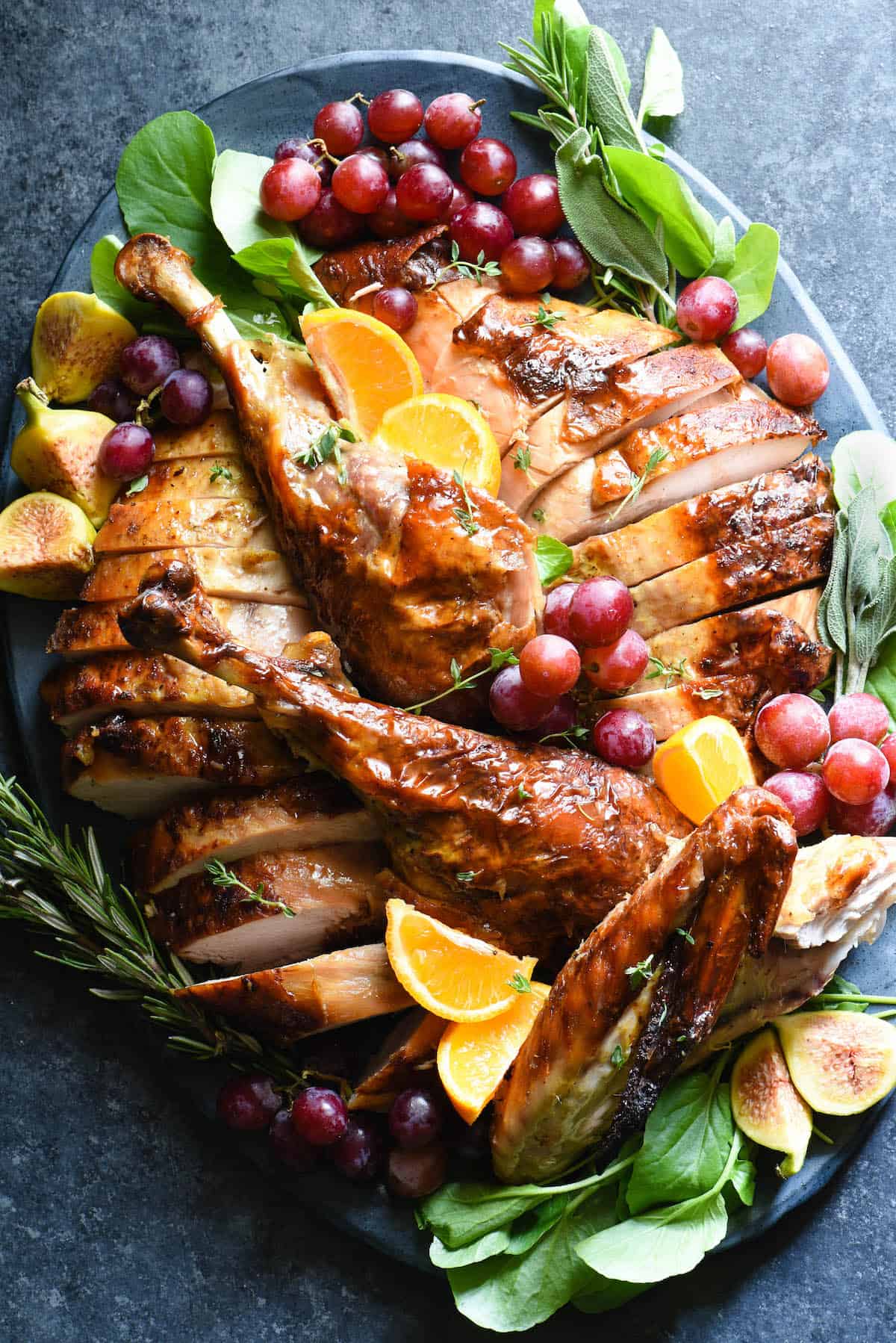 Large slate blue ceramic platter filled with a cut up roasted turkey, garnished with grapes, orange slices and herbs.