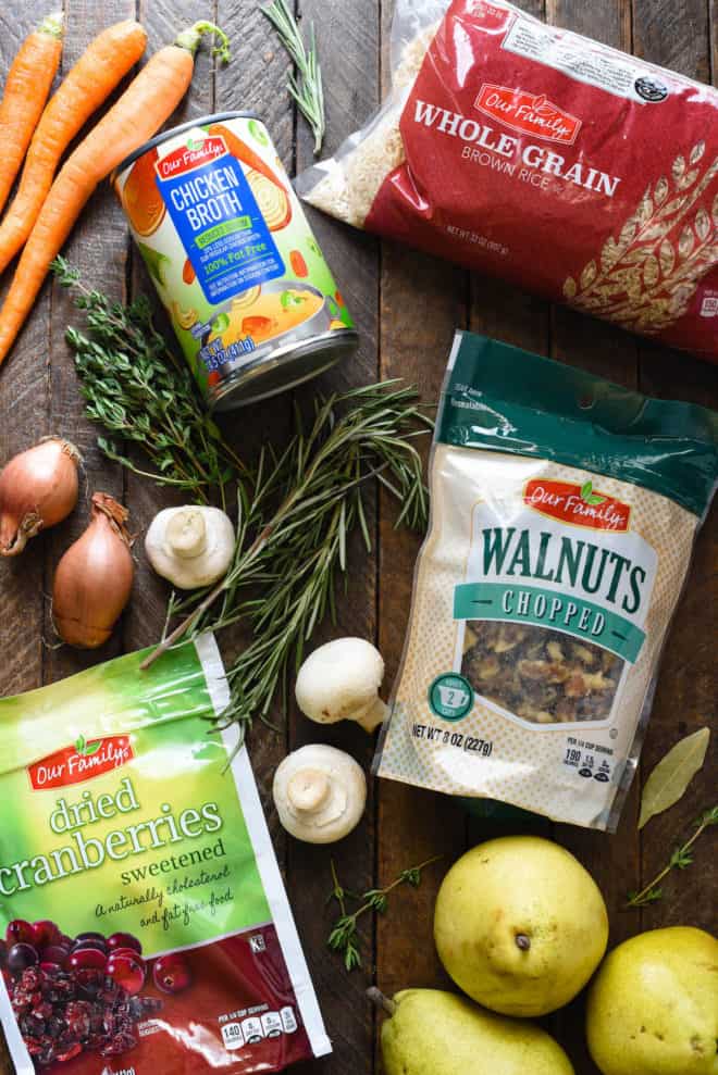 Ingredients on a wooden surface, including walnuts, dried fruit, rice, herbs, mushrooms, pears, and carrots.