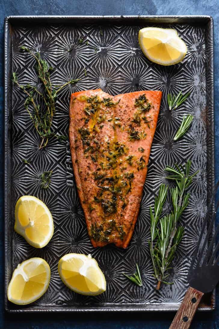 A piece of roasted pink fish topped with herbs on texture baking pan.