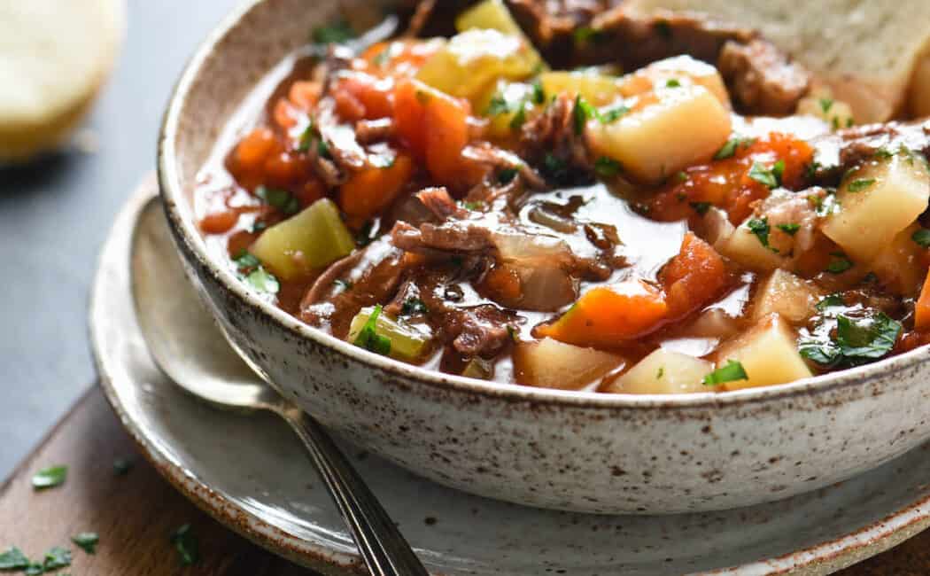 Bowl of vegetable soup with beef, with piece of white bread dunked into it.