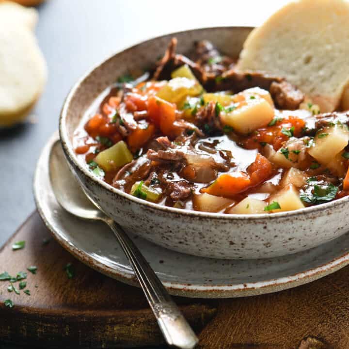 Bowl of vegetable soup with beef, with piece of white bread dunked into it.