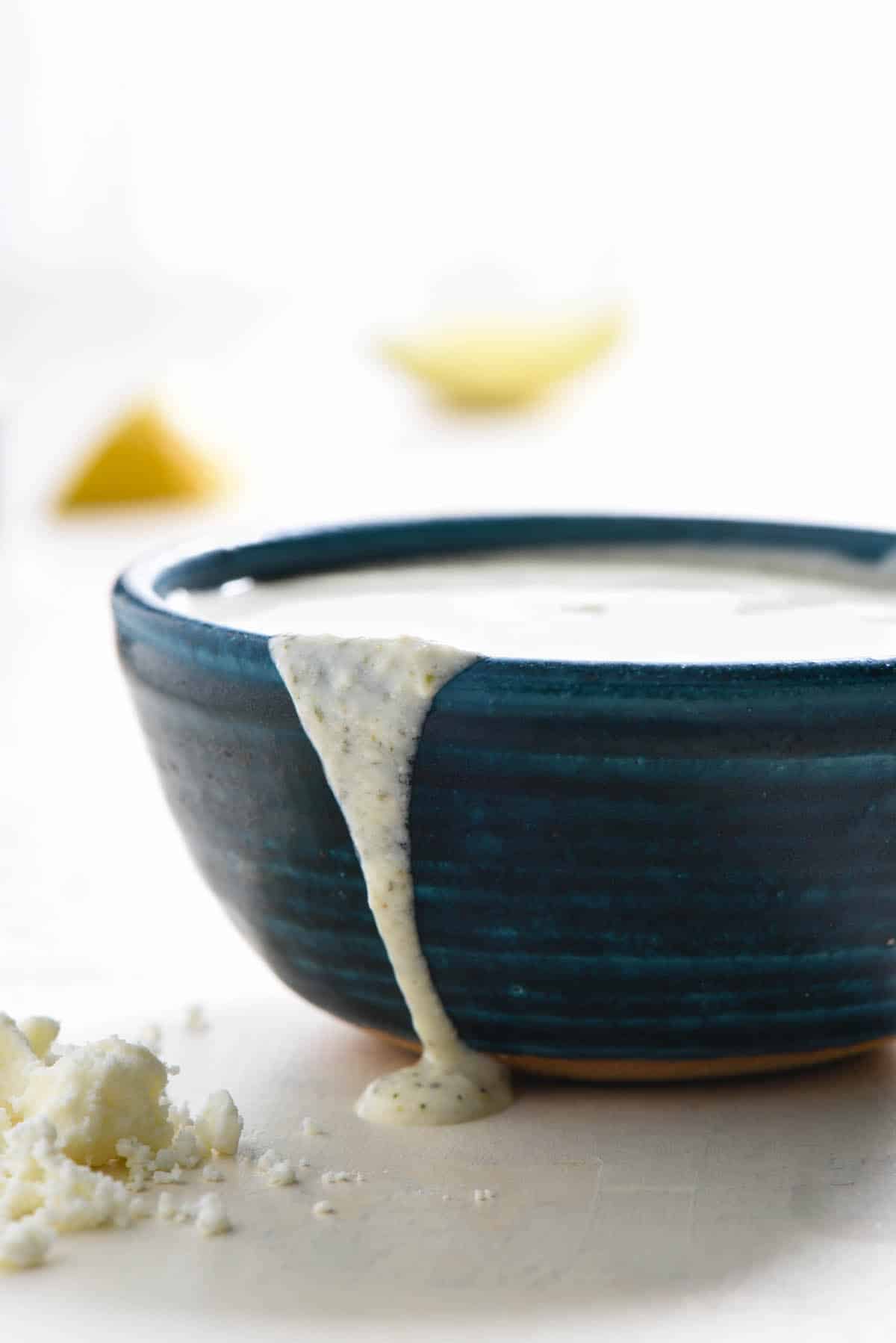 A small blue bowl overflowing with a white sauce.