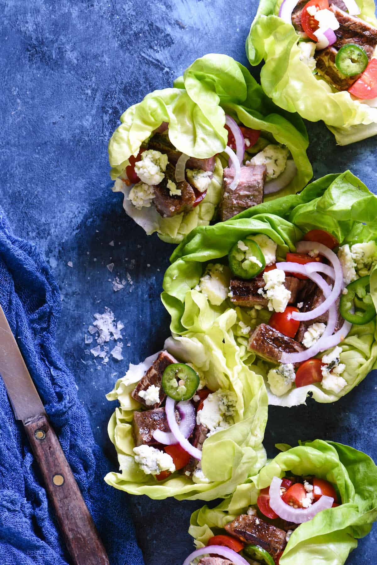 Butter lettuce leaves filled with steak, blue cheese, tomatoes and onions on a blue background.