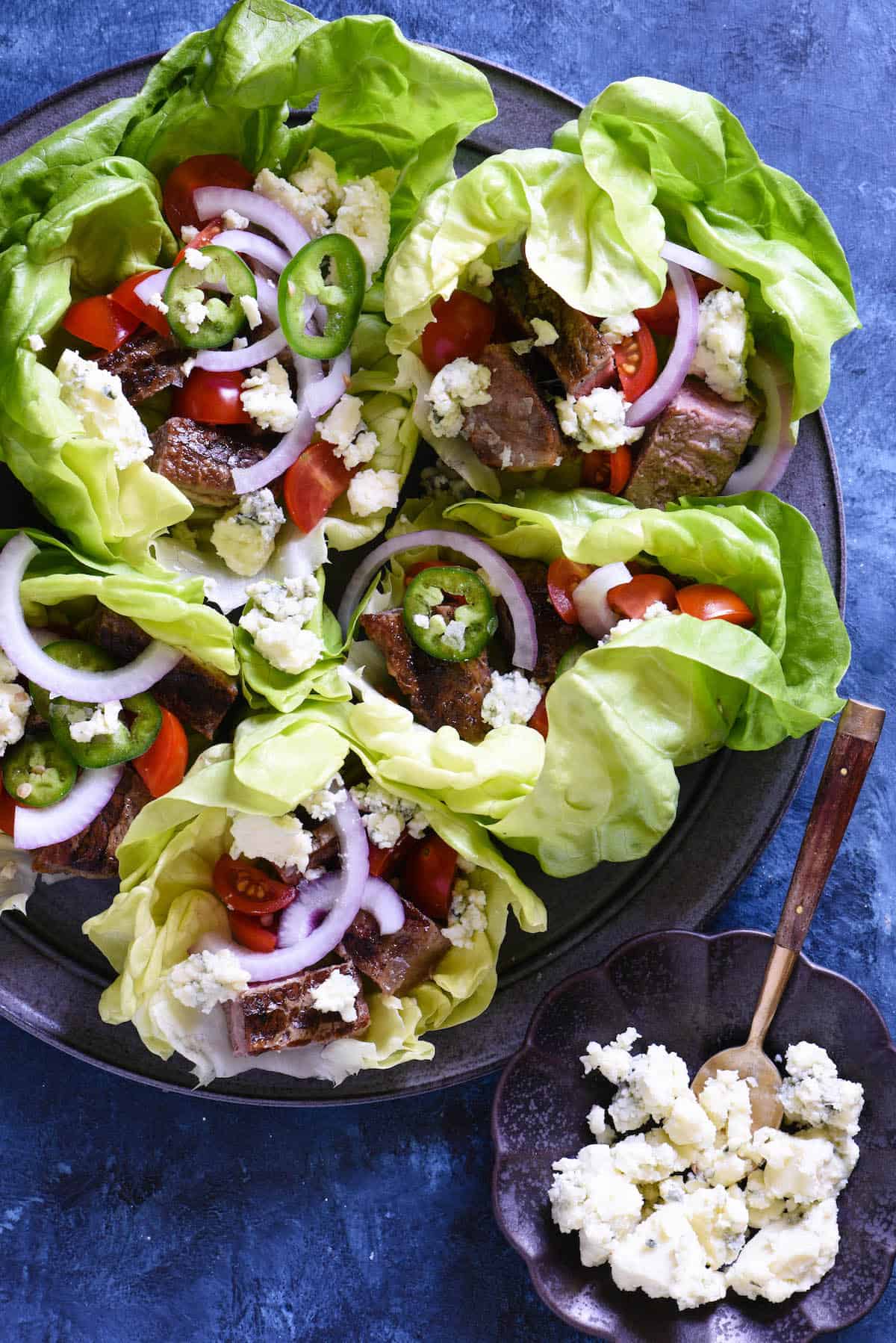 Beef wrapped in lettuce with blue cheese, tomatoes and onions on a gray plate on a blue background.