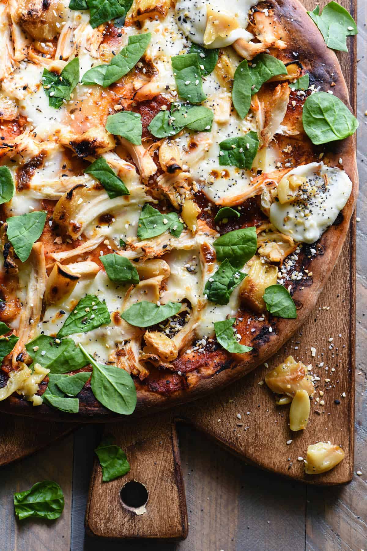 Pizza topped with mozzarella, chicken, roasted garlic and spinach, on wooden cutting board.