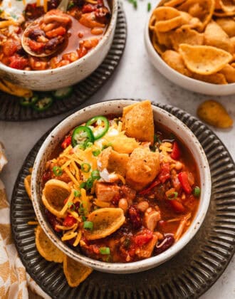 A bowl of the best turkey chili recipe topped with corn chips, cheese, sour cream and green onions.