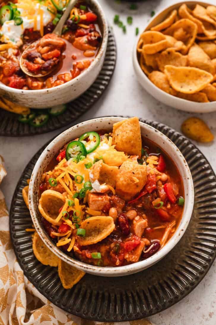 A bowl of the best turkey chili recipe topped with corn chips, cheese, sour cream and green onions.