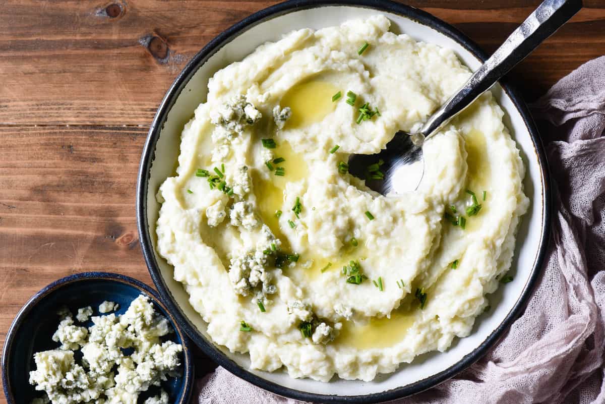 A shallow bowl filled with gorgonzola mashed potatoes garnished with melted butter and chives.