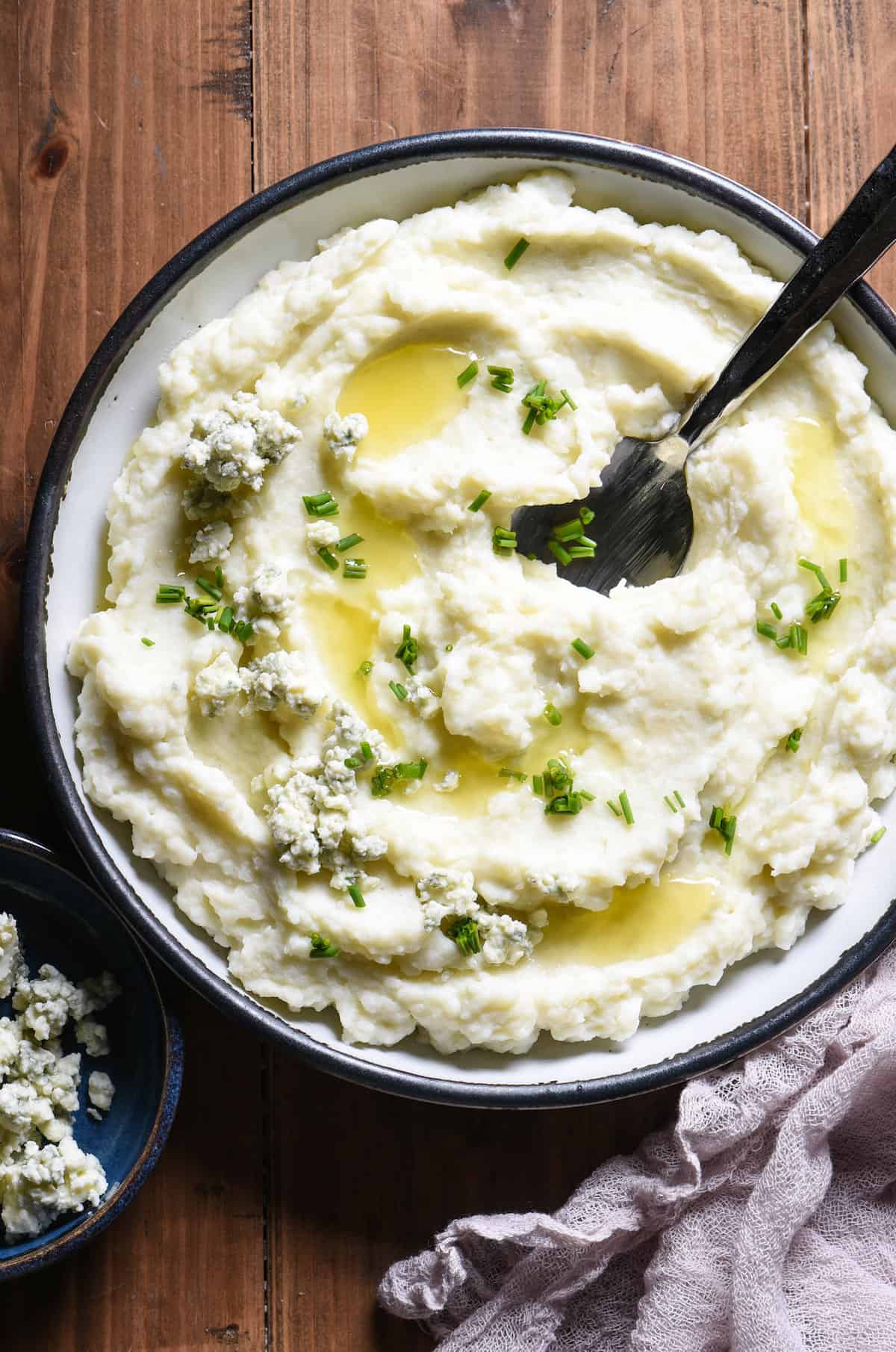 A shallow bowl filled with blue cheese mashed potatoes garnished with melted butter and chives.