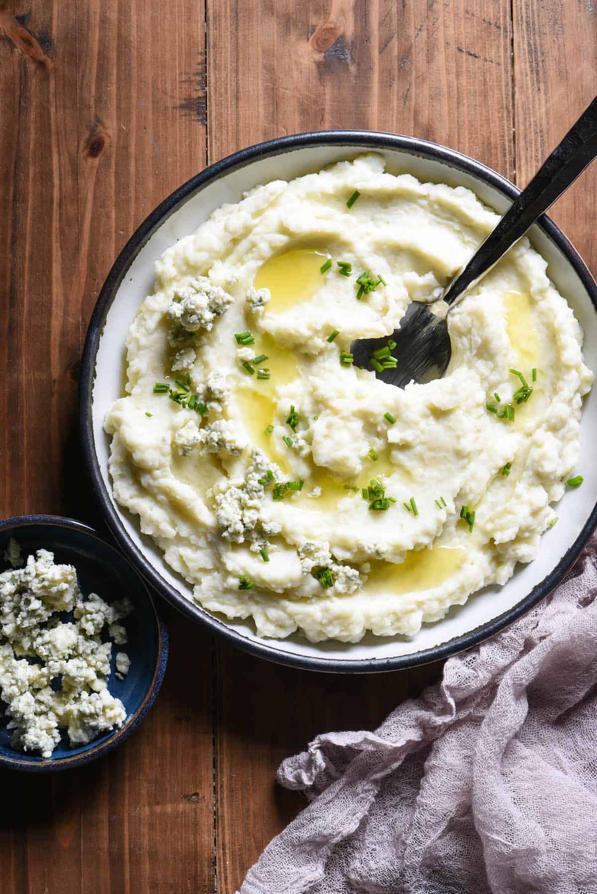 A shallow bowl filled with blue cheese mashed potatoes garnished with melted butter and chives.