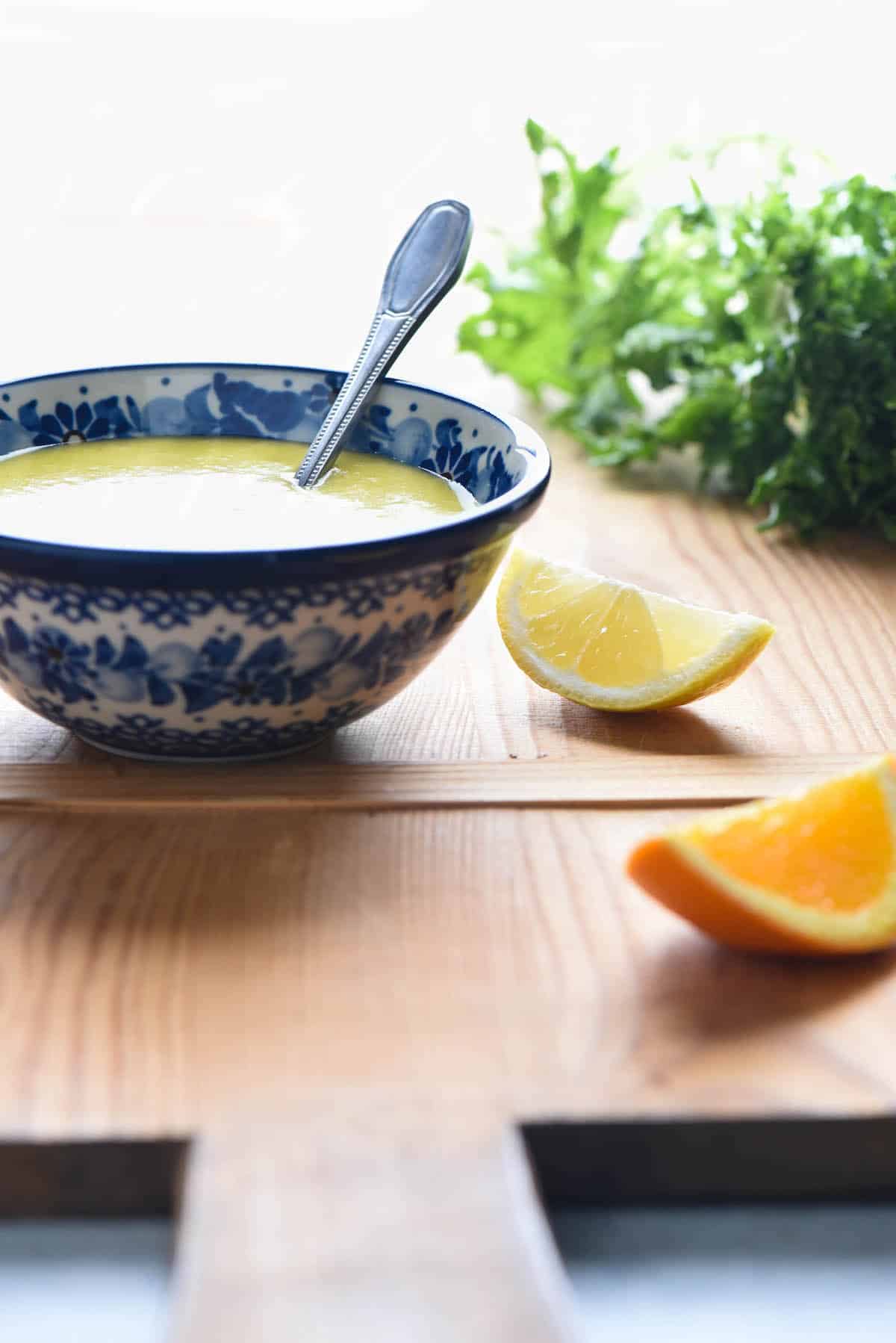 A small painted blue bowl filled with citrus salad dressing with a spoon in it.