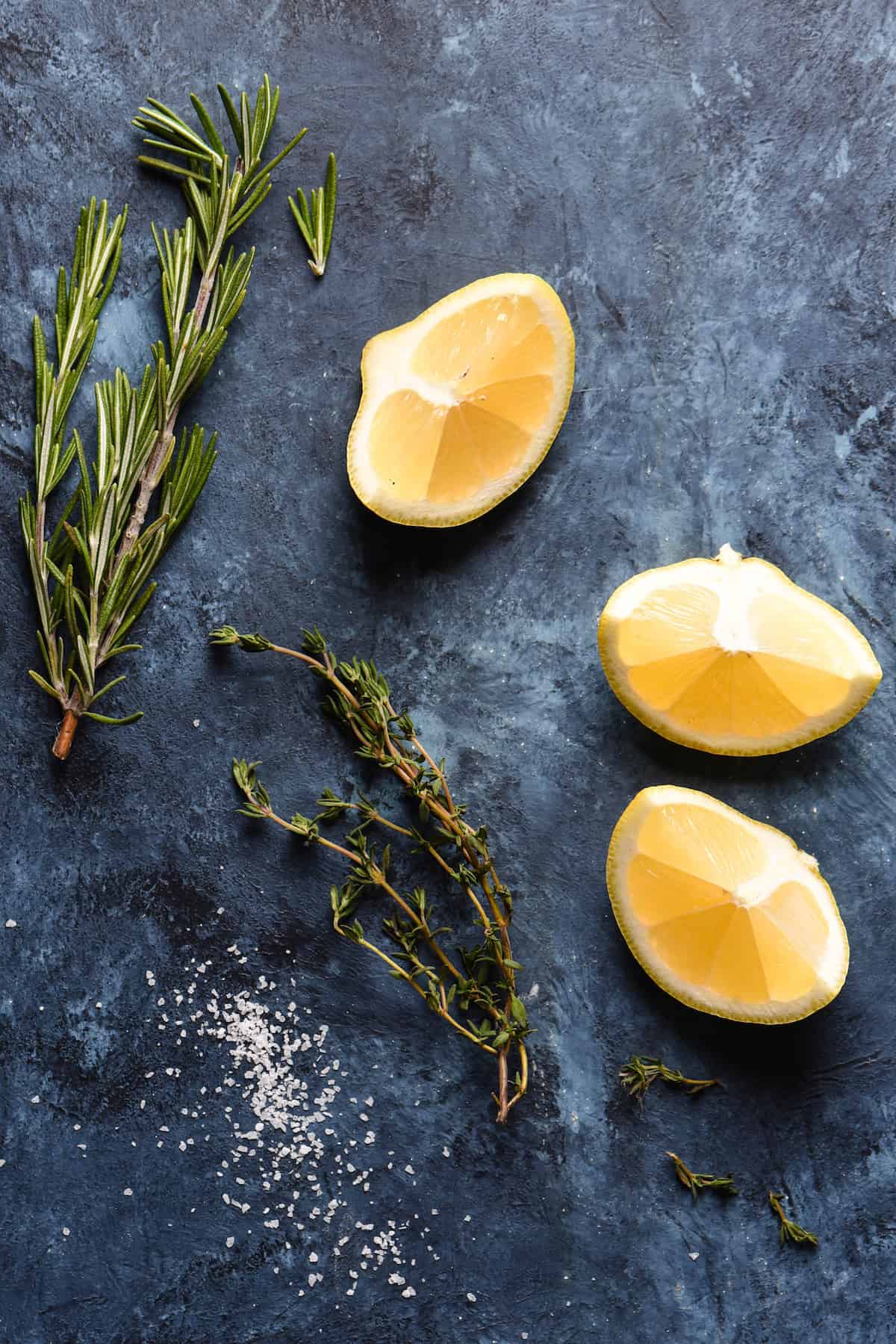 Lemon wedges, rosemary and thyme sprigs and salt, on blue background.