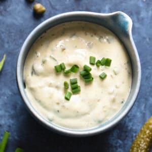 A small blue bowl filled with homemade tartar sauce garnished with chopped chives.