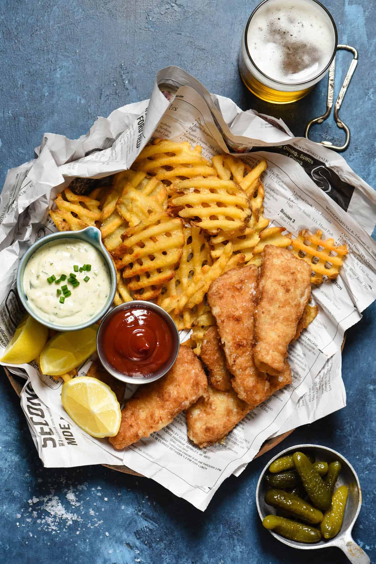 A basket of fried fish and waffle fries with ramekins of ketchup and  a homemade tartar sauce recipe.