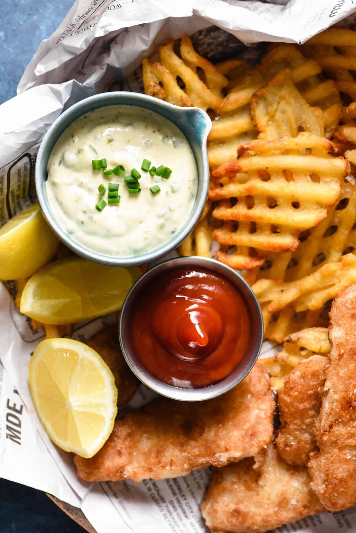 A basket of fried fish and waffle fries with ramekins of ketchup and a recipe for tartar sauce.