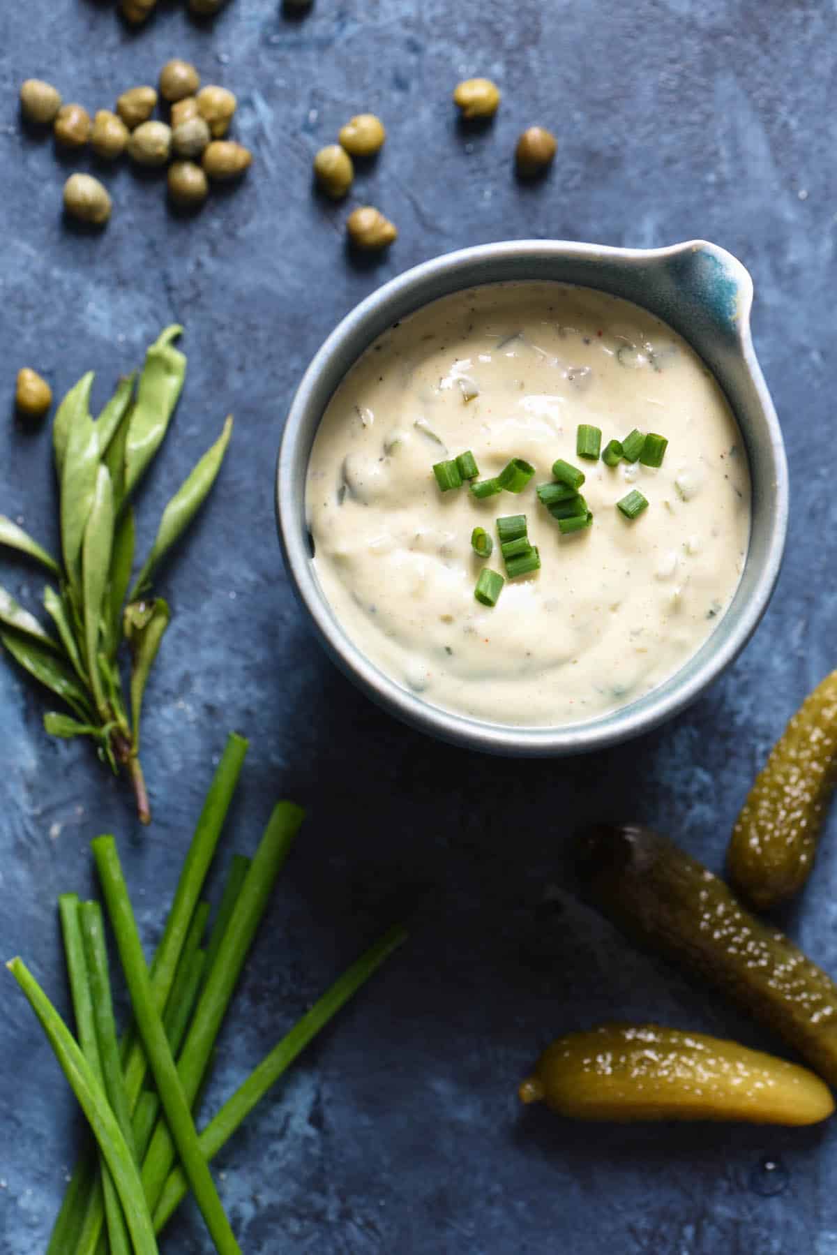 A small blue bowl filled with homemade tartar sauce garnished with chopped chives.