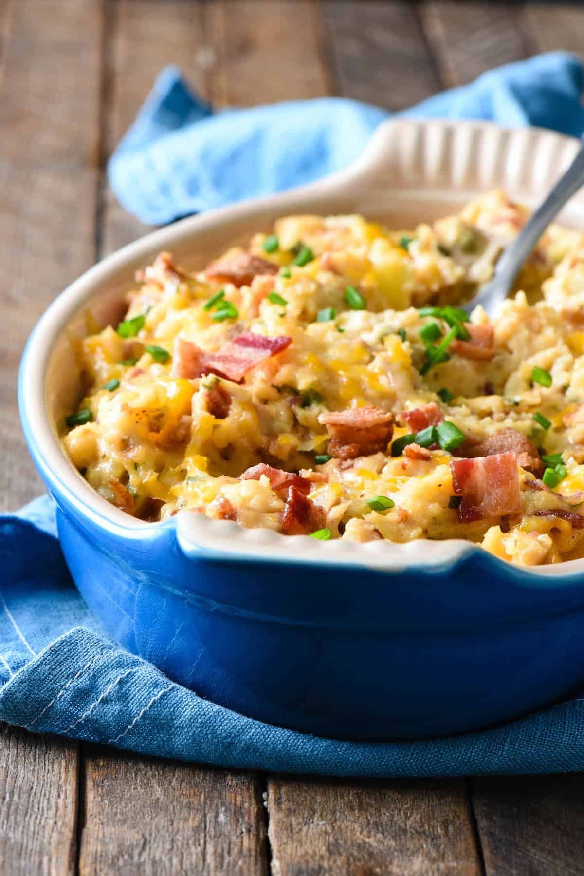 Mashed potato casserole with bacon and green onions, in oval blue baking dish.
