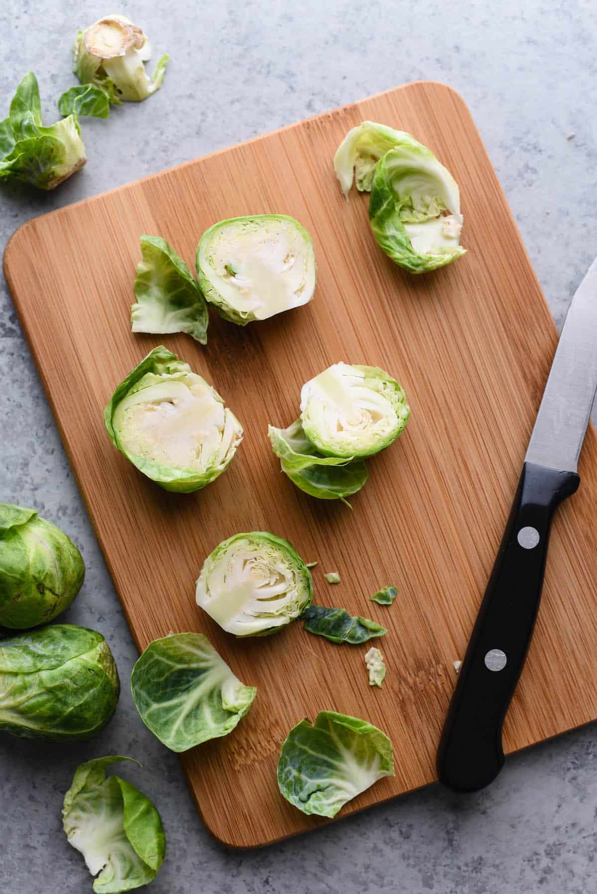 Halved raw brussels sprouts on cutting board with paring knife.