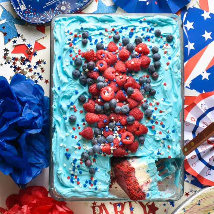 Overhead shot of red white and blue ice cream cake with one piece cut and turned. Cake is topped with berries and sprinkles.