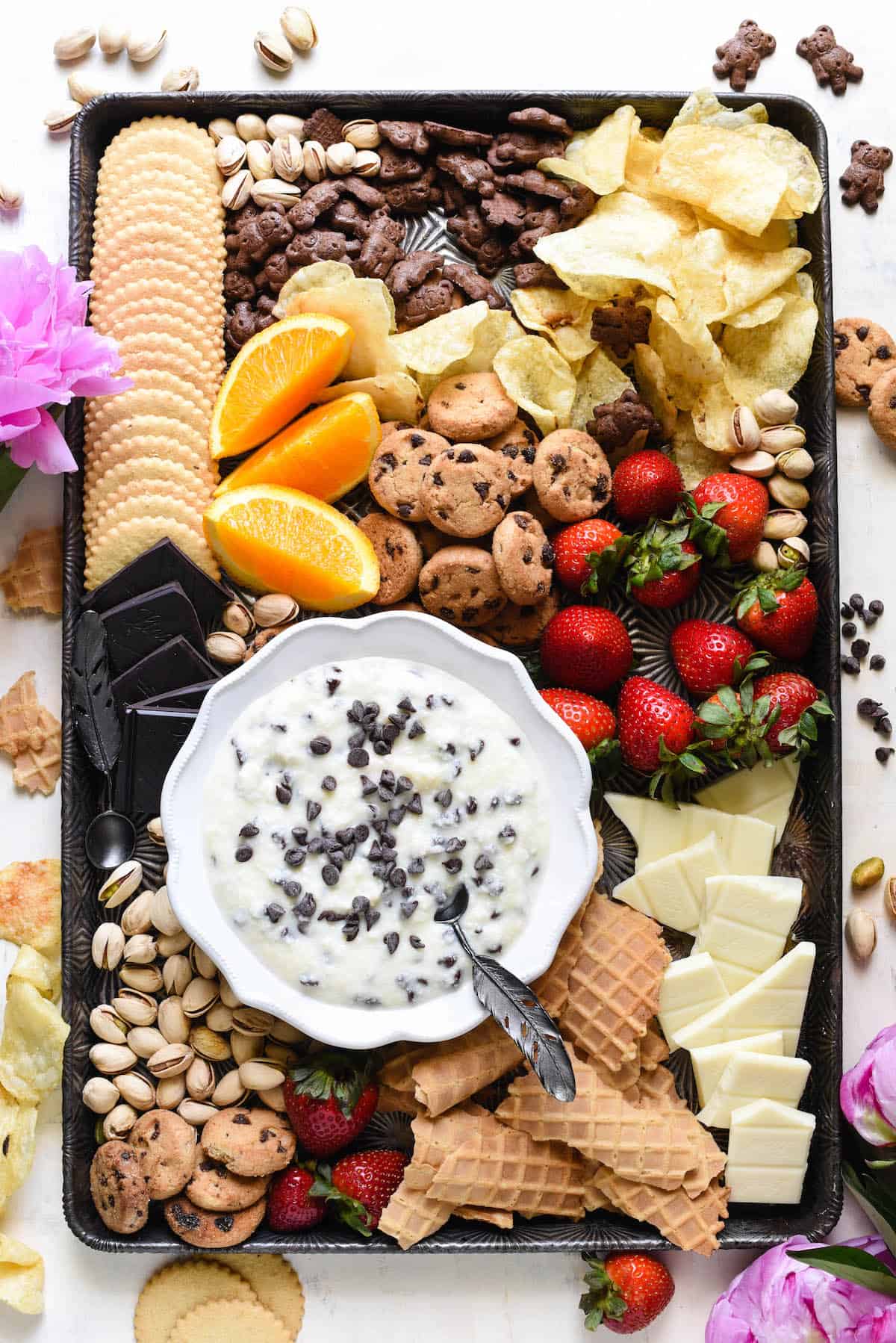 Overhead shot of large pan with bowl of cannoli dip and cookies, fruit, nuts and potato chips for dipping.