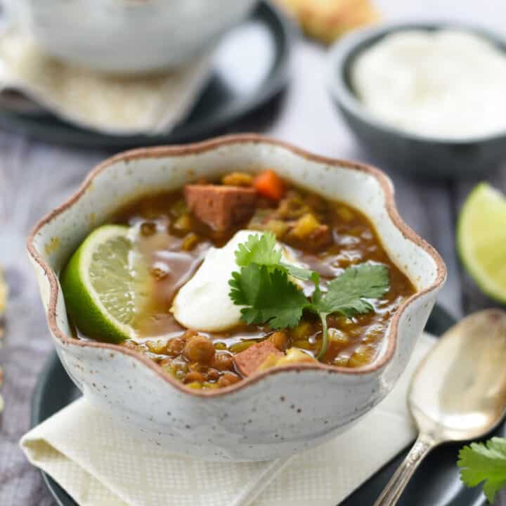 Two fluted rustic bowls of Instant Pot lentil soup topped with yogurt, cilantro and limes wedges.