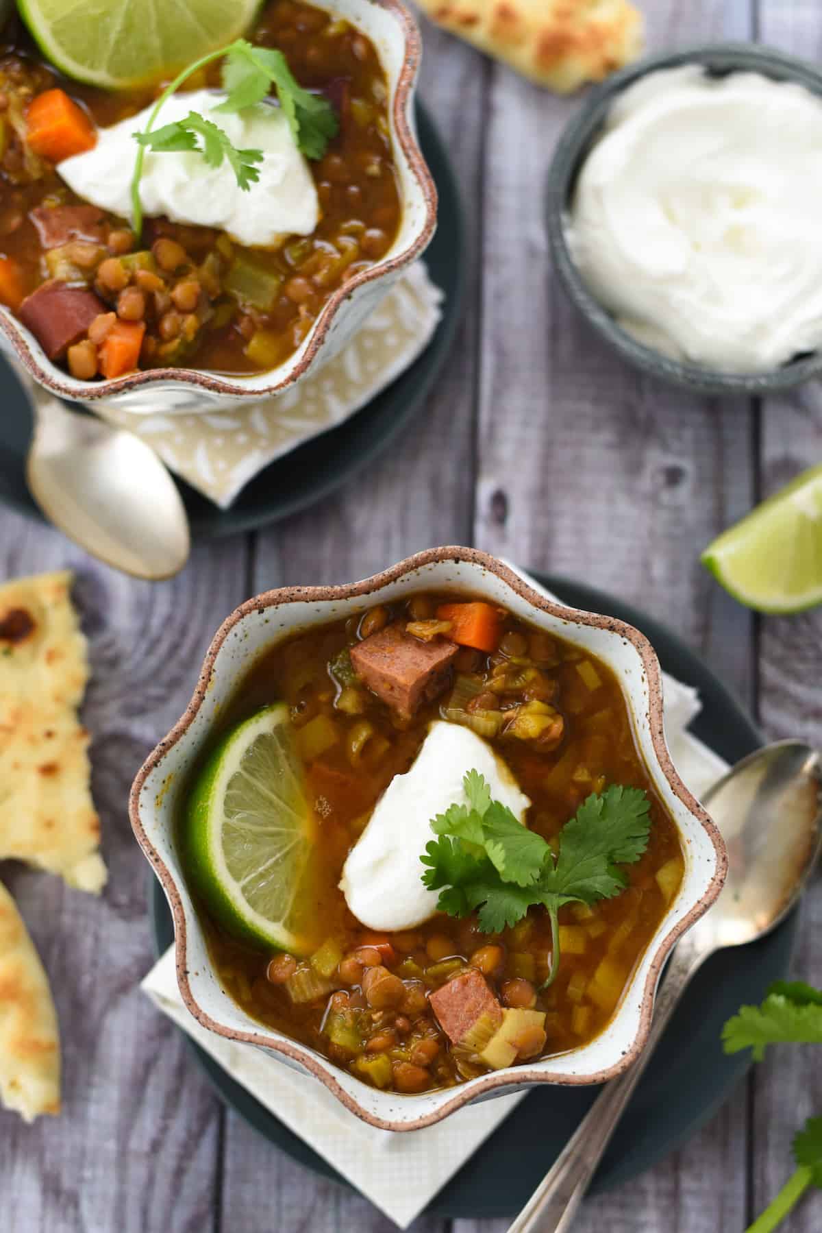 Overhead photos of two bowls of soup with lentils and sausage, with bowl of yogurt and naan bread alongside.