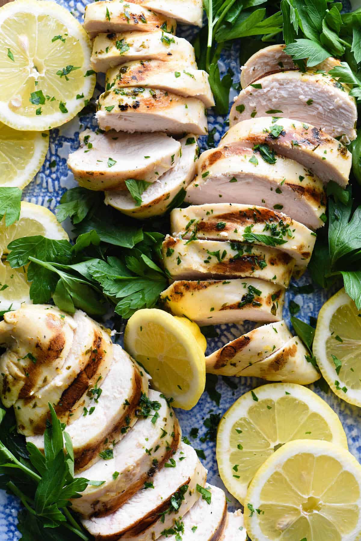 Sliced grilled chicken breasts with lemon slices and parsley.