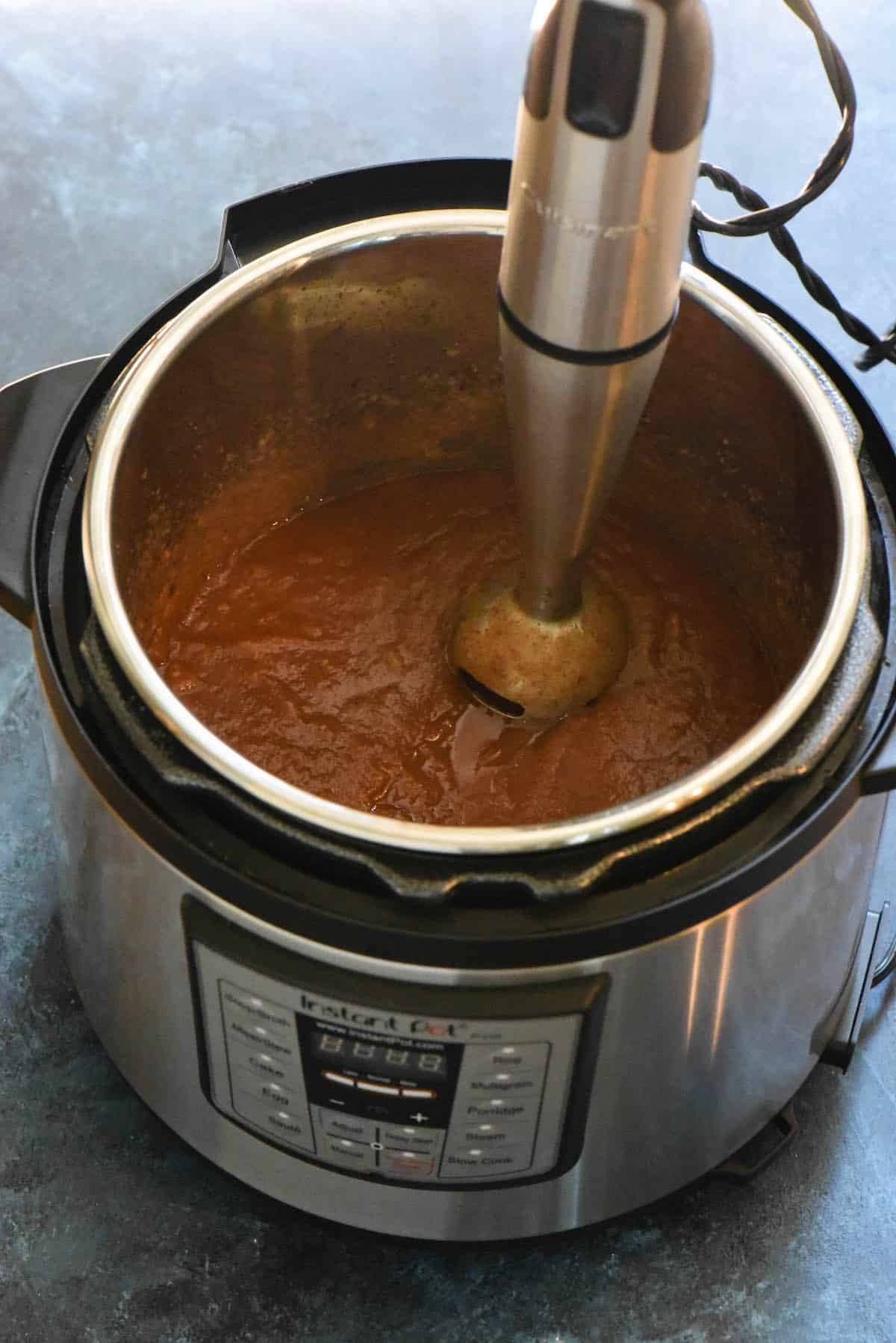 Apple butter being pureed in Instant Pot with immersion blender.
