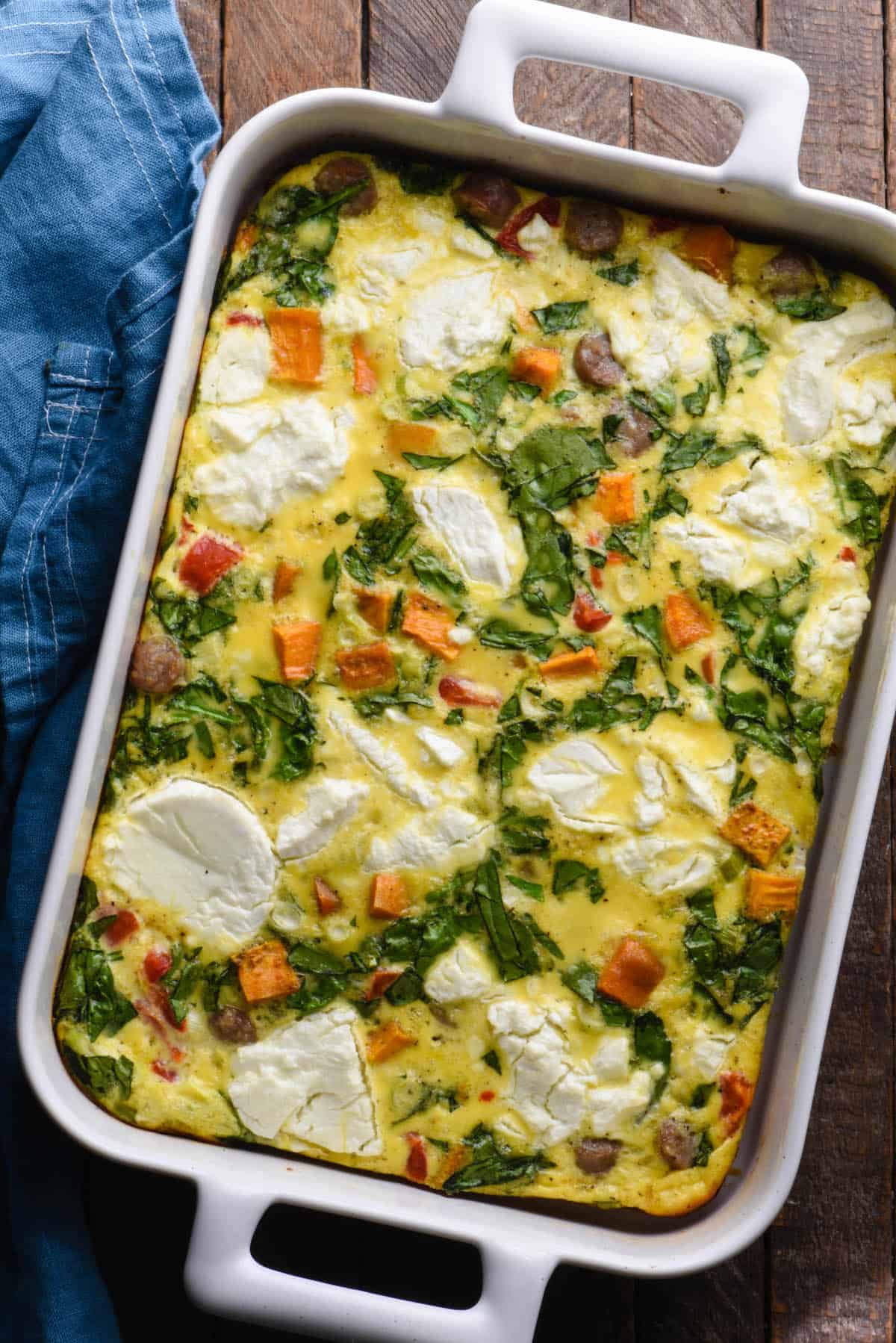 Egg bake made with sweet potatoes, sausage, spinach and goat cheese, in rectangular white baking dish.