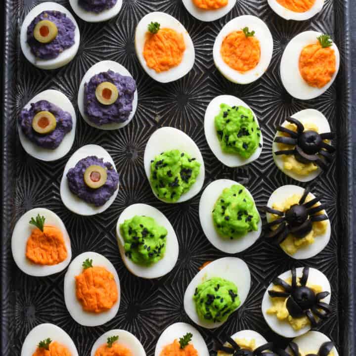 Cookie sheet with various types of Halloween decorated deviled eggs arranged on top.