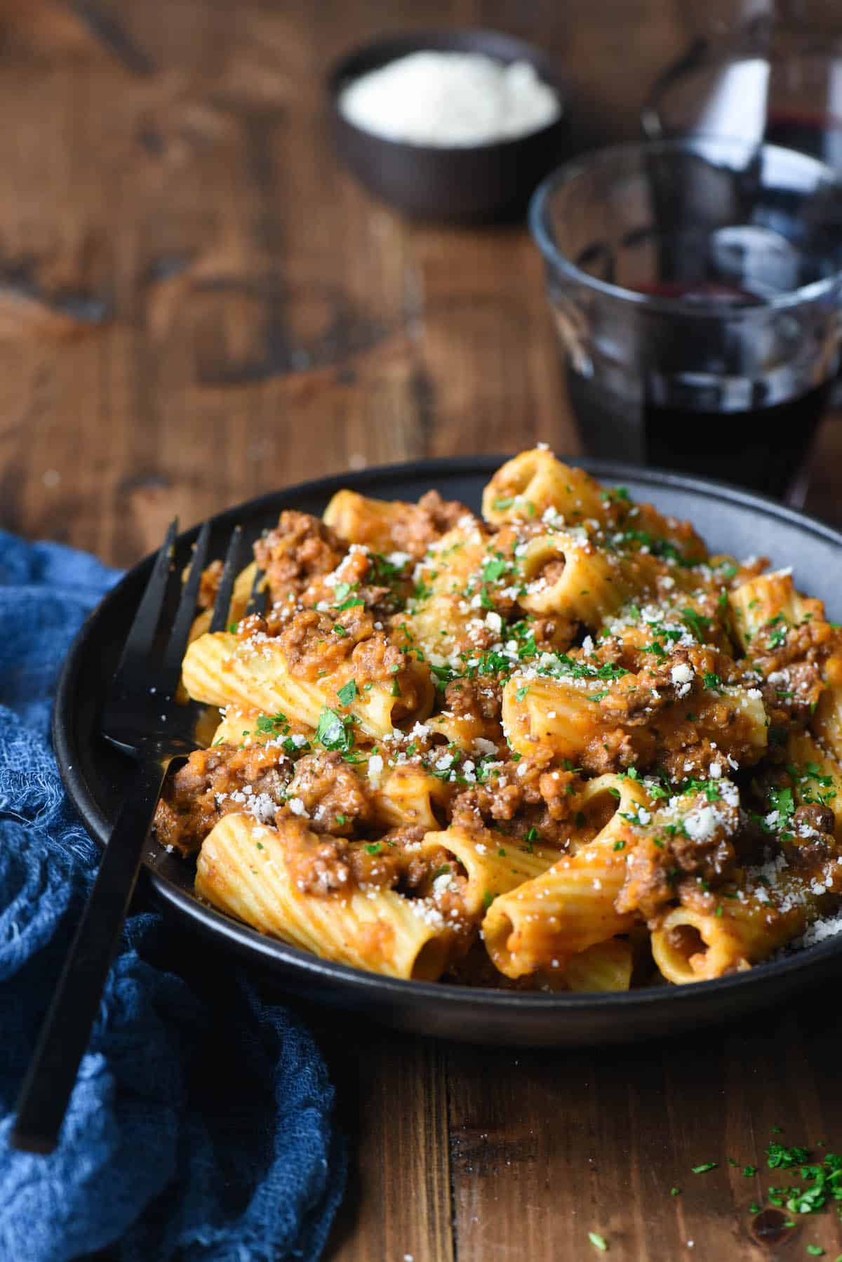 Black bowl filled with rigatoni alla bolognese, with black fork digging in.