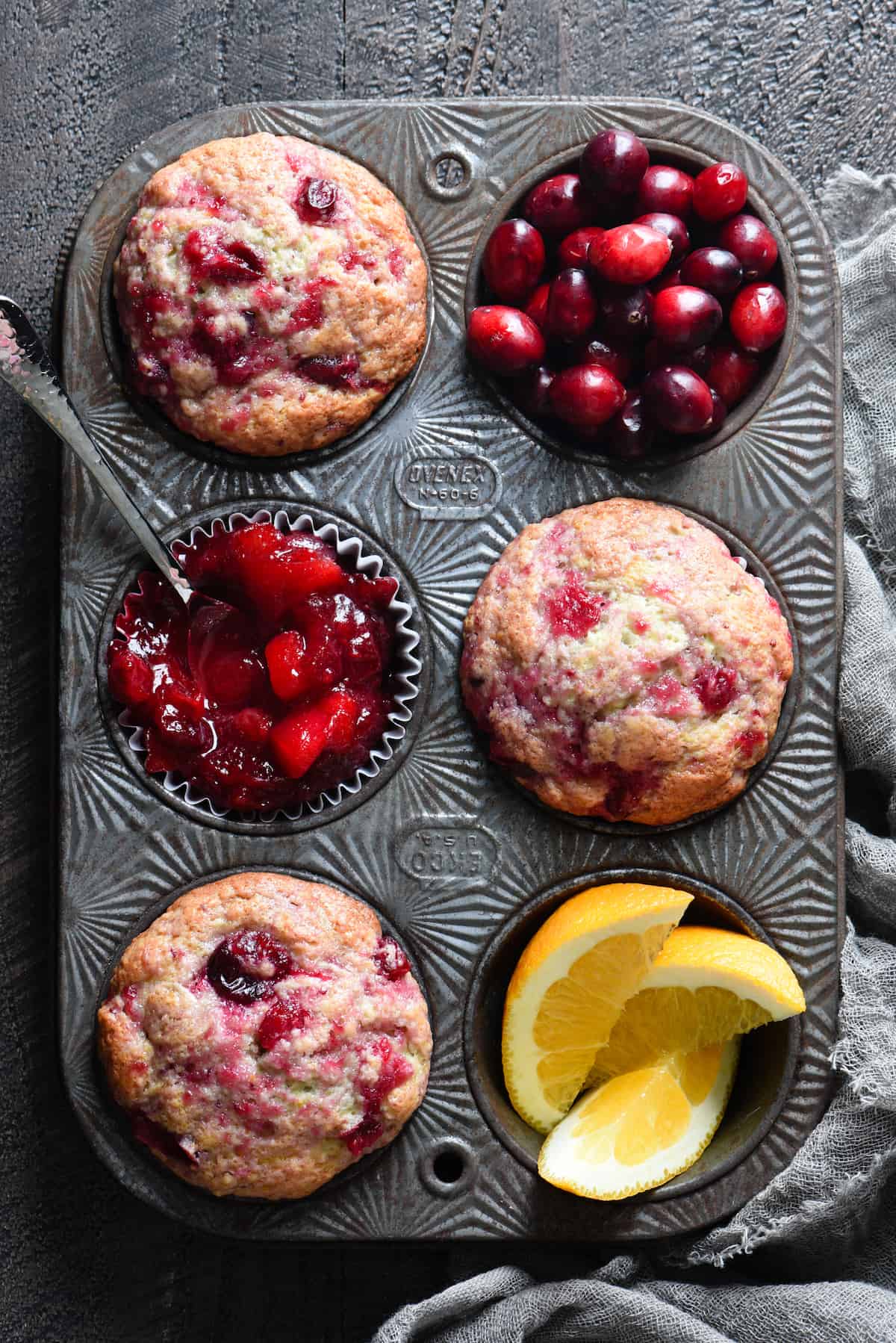 Overhead photo of muffin pan filled with three muffins, fresh cranberries, cranberry sauce and orange slices.