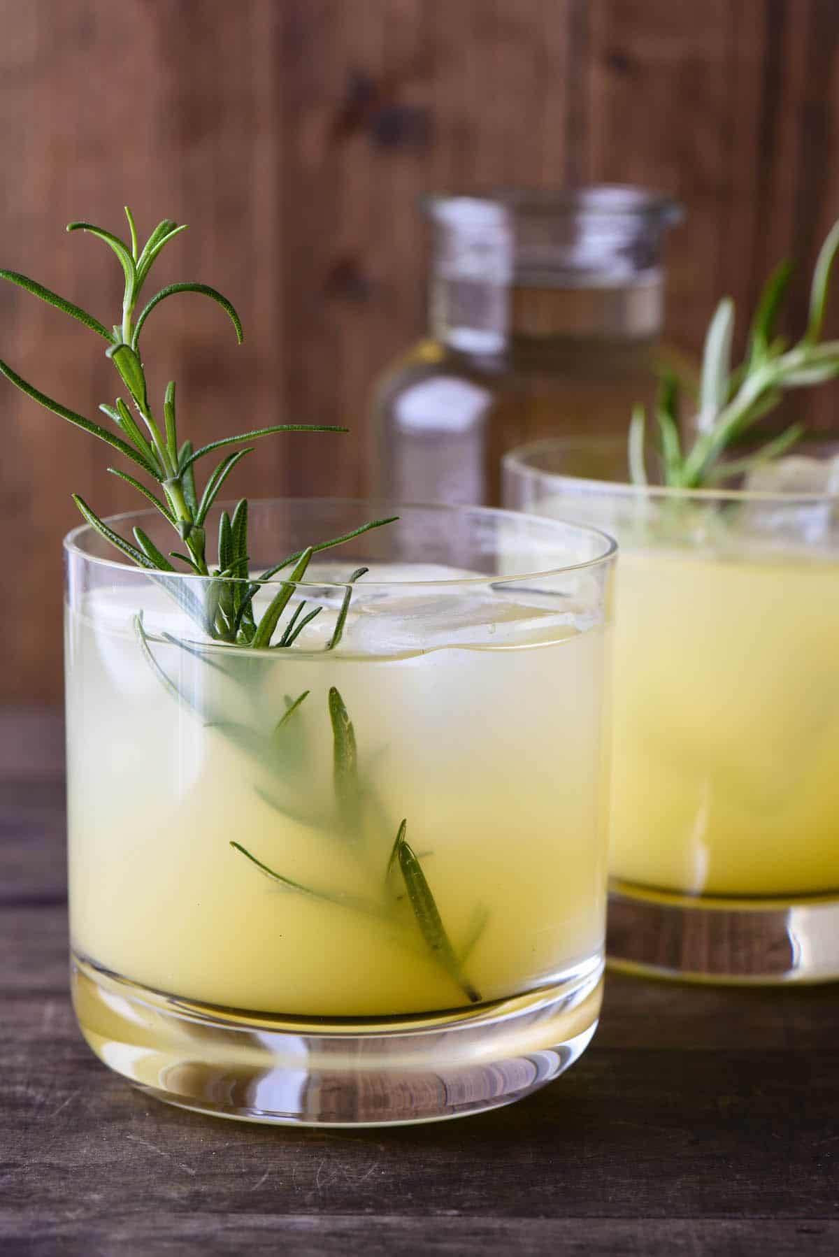 Orange hued cocktail in small glass with a rosemary sprig garnish.
