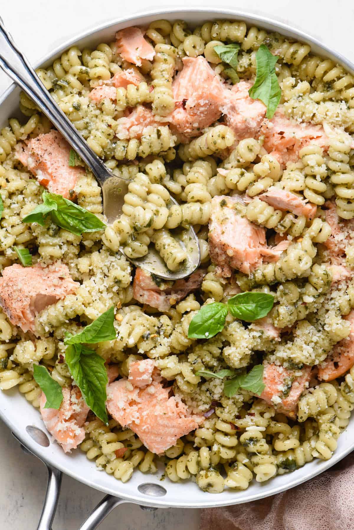 Closeup photo of salmon pasta with pesto, in white skillet.