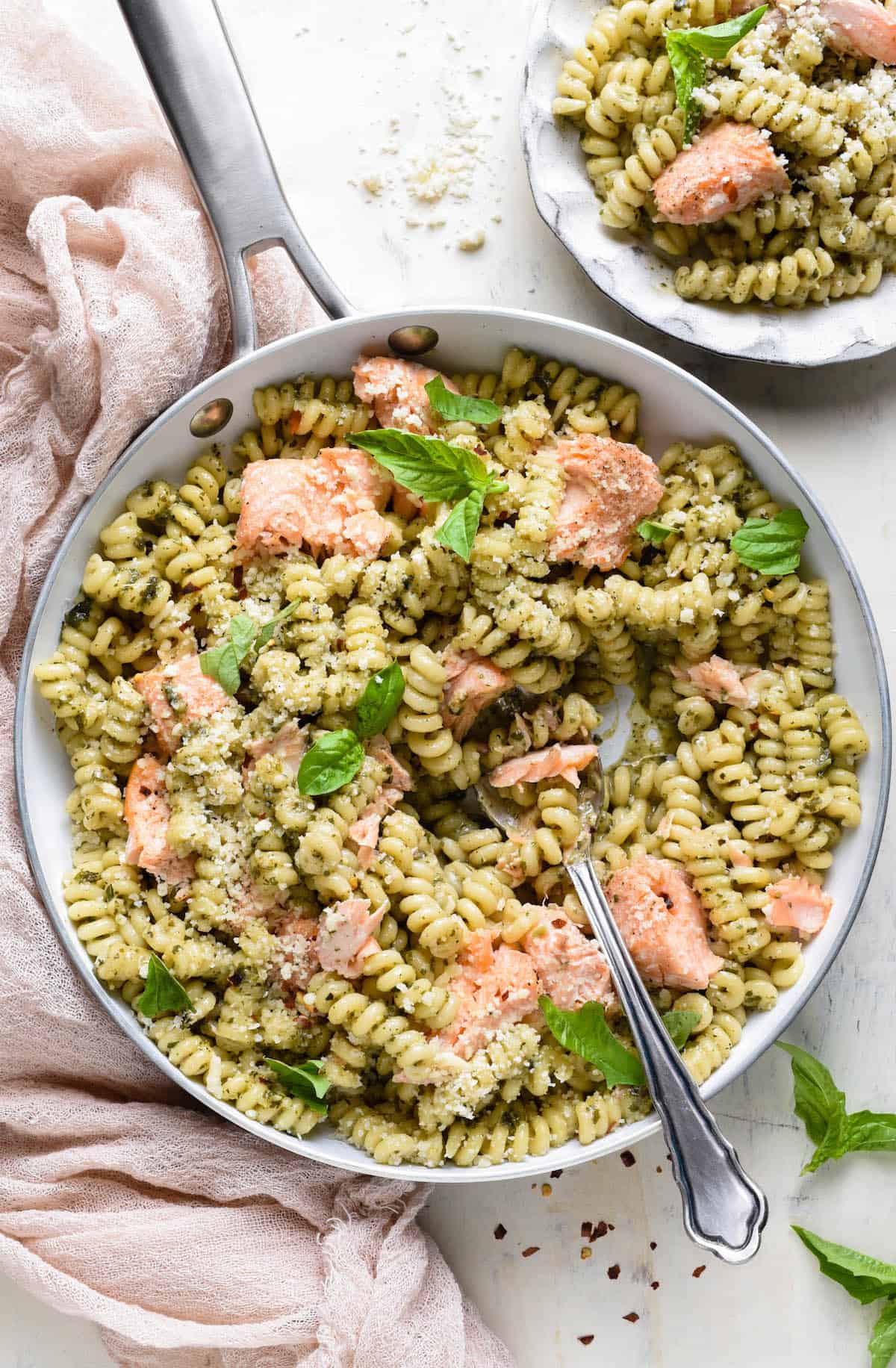 Overhead photo of skillet filled with spiral shaped noodles tossed with pesto, and chunks of salmon.