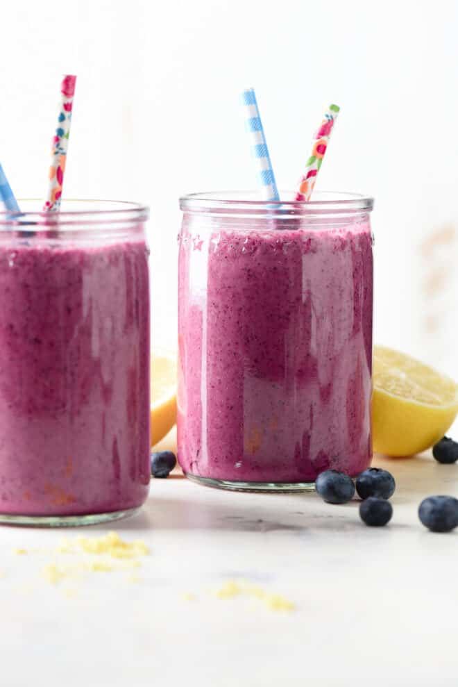 Two glass jars filled with bright purple blended fruit drink and fun straws.