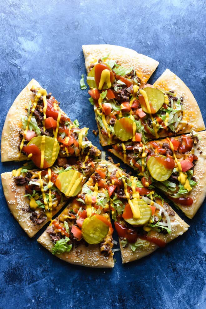 Overheat photo of cut cheeseburger pizza, missing one slice, on blue background.