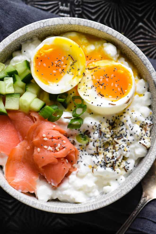 Closeup on savory cottage cheese breakfast bowl topped with soft egg, lox, cucumber and green onion.