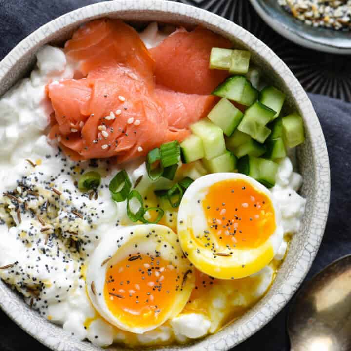 Gray bowl filled with cottage cheese, soft egg, smoked salmon and green onions.