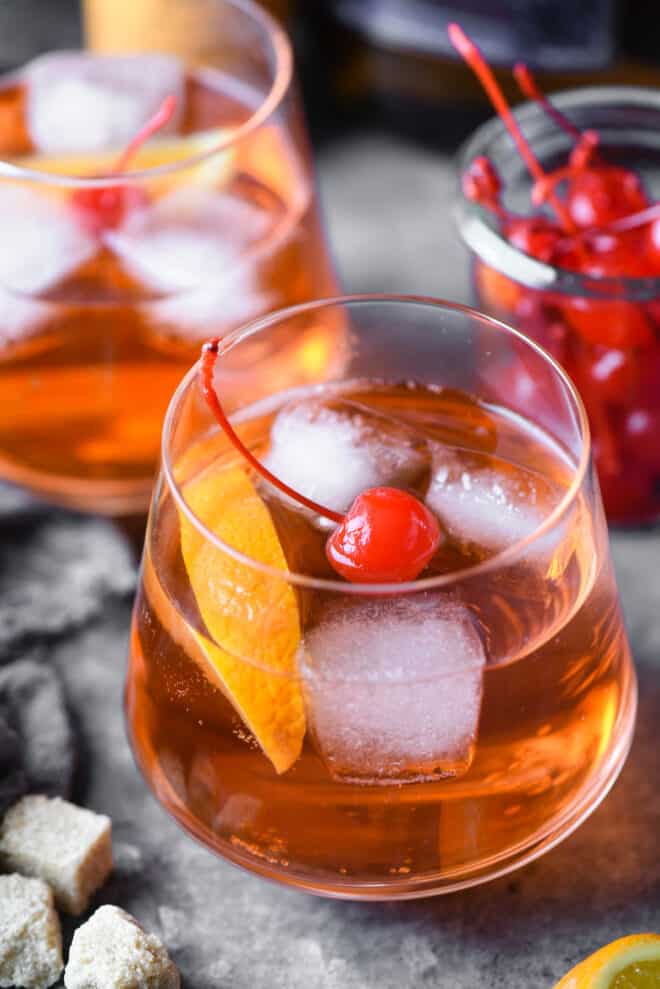 Closeup on a brandy old fashioned cocktail garnished with an orange slice and maraschino cherry.