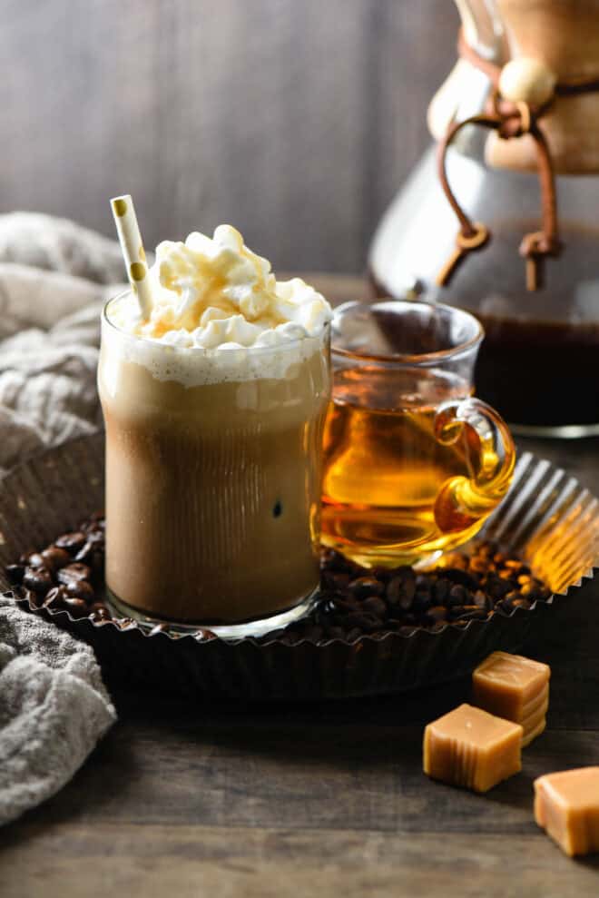 Small glass of iced coffee drink topped with whipped cream and caramel sauce, with a straw.