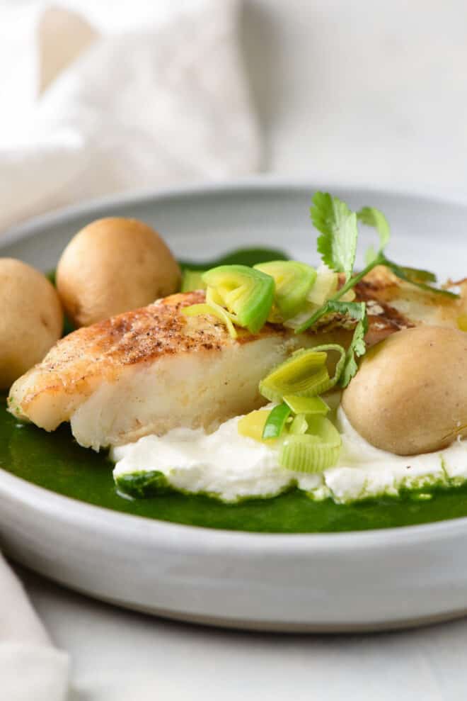 Pan seared Chilean sea bass, topped with leeks and cilantro, with yogurt, green sauce and potatoes.