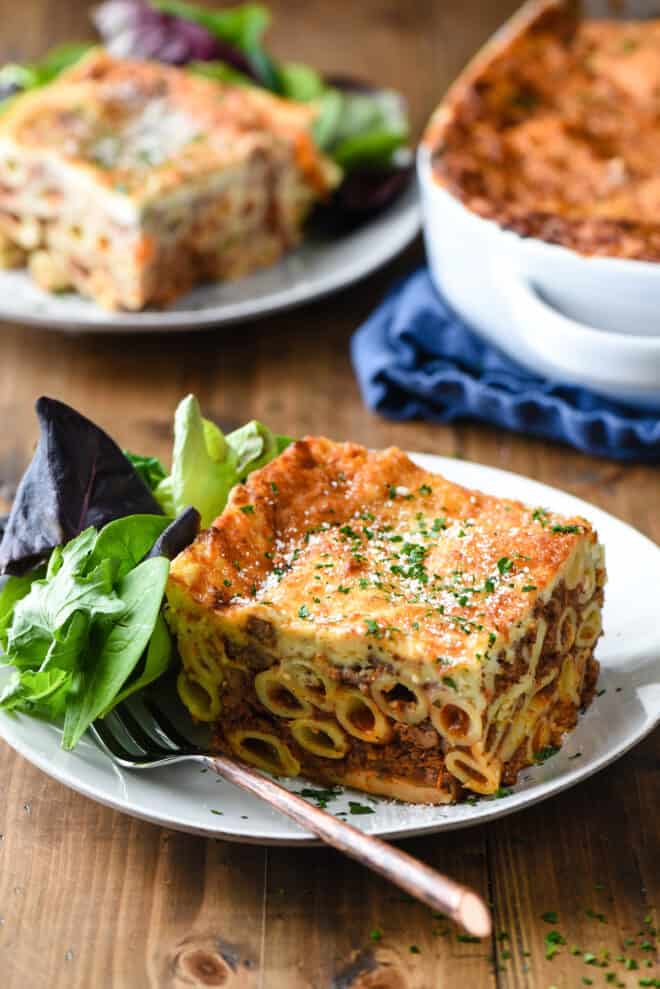 Square piece of Greek lasagna on plate with salad and fork.