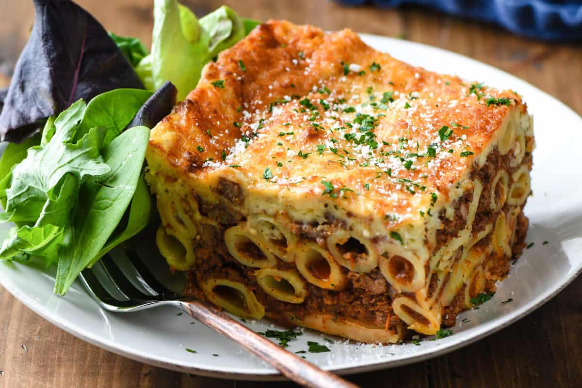 Large slice of Greek lasagna on white plate with green salad.