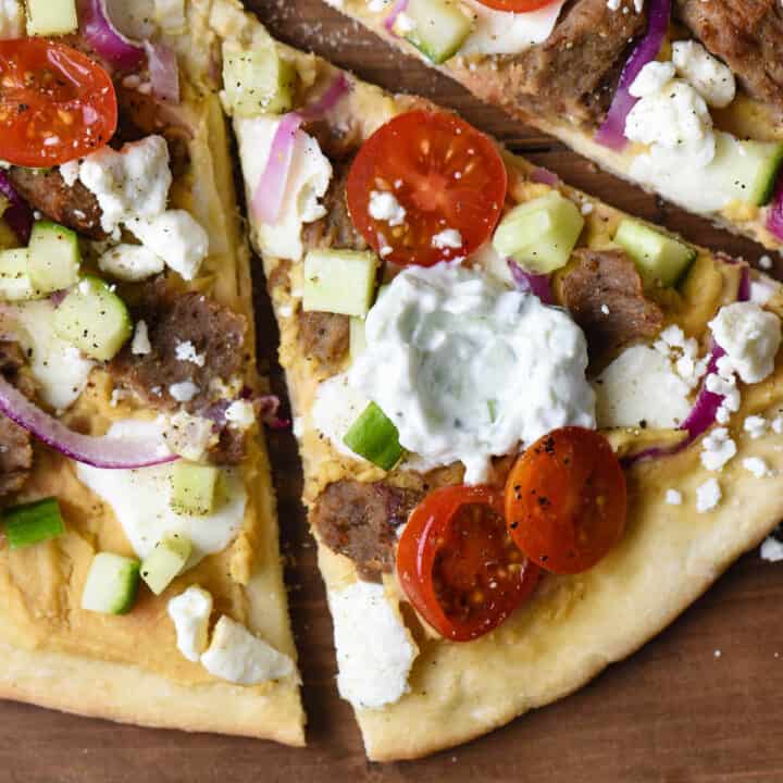 Closeup on slice of pizza topped with gyro meat, vegetables, and tzatziki sauce.